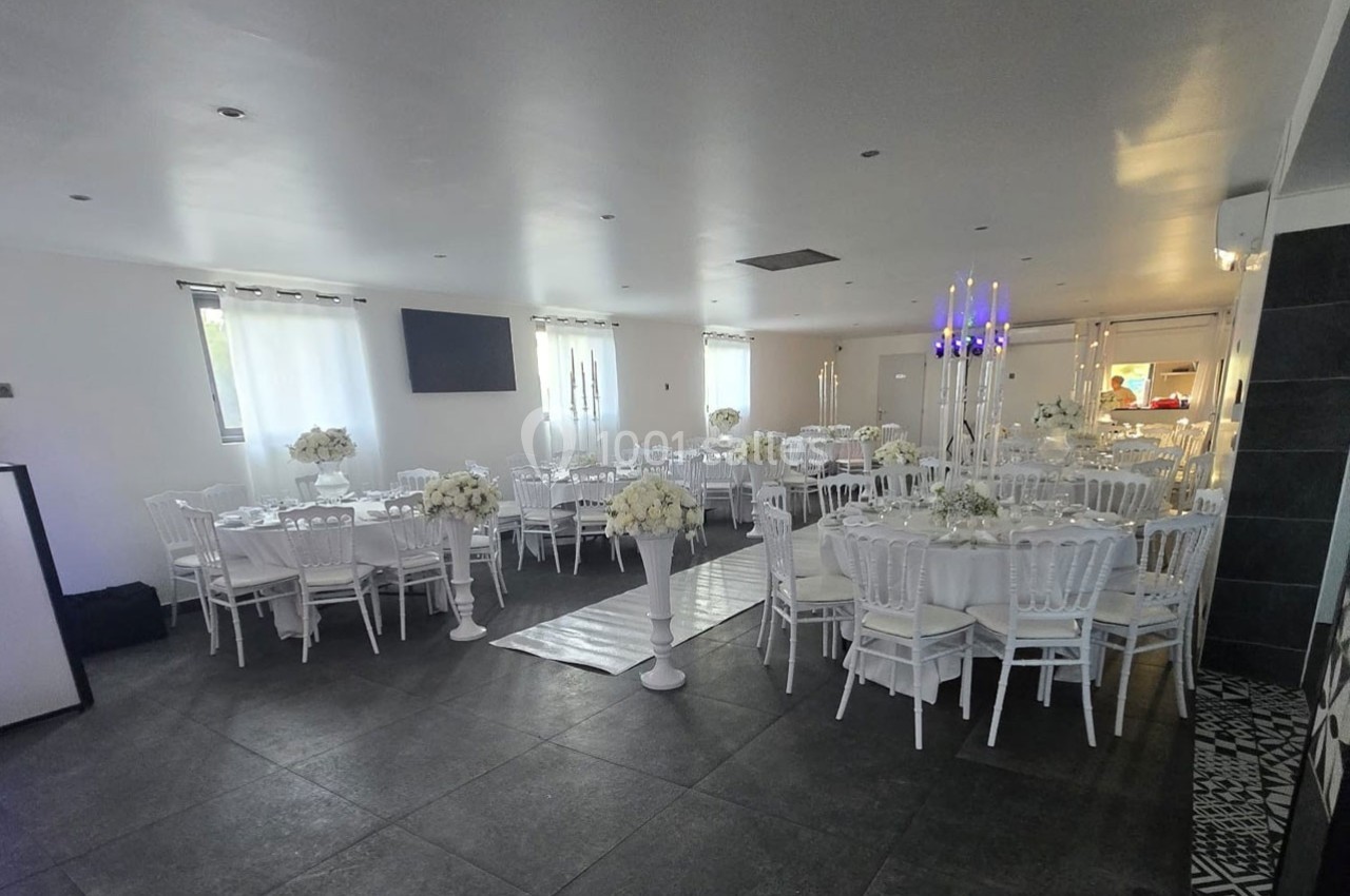 Salle de réception décorée avec des tables rondes, nappes blanches, chaises assorties et arrangements floraux élégants.