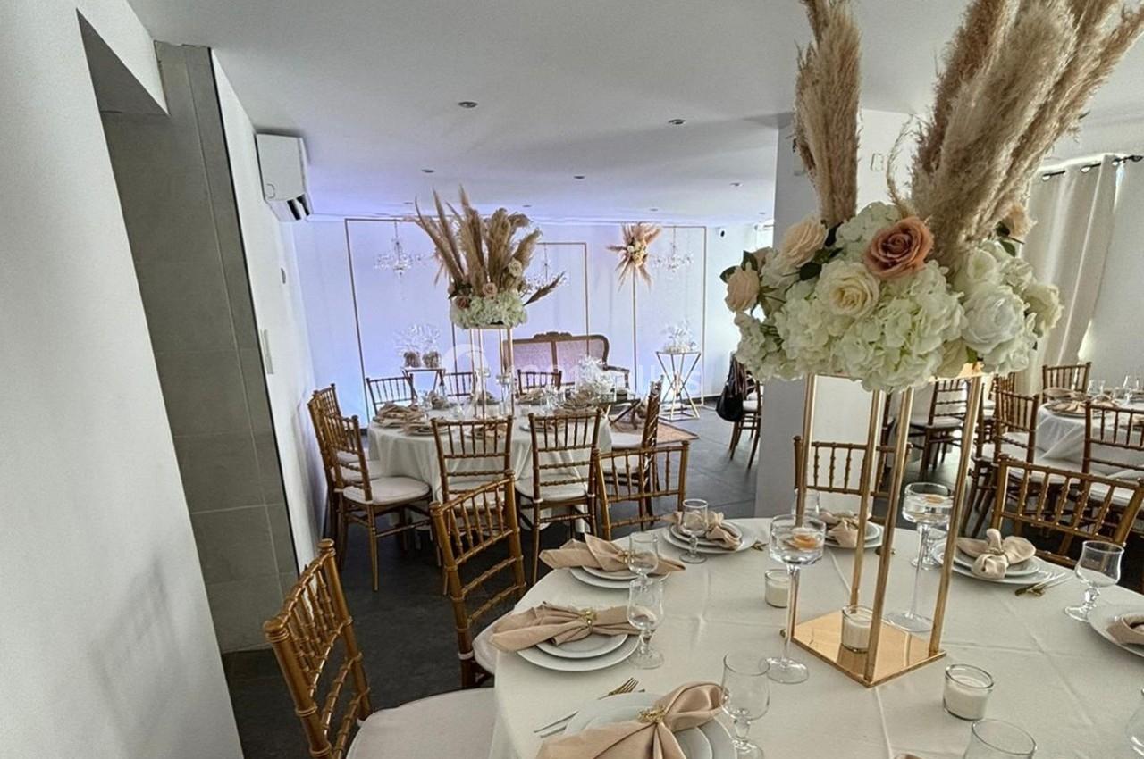 Salle de réception décorée avec des tables rondes, nappes blanches, chaises dorées et arrangements floraux élégants.