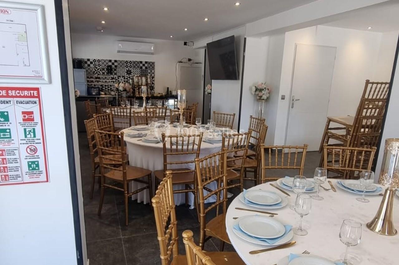 Salle de réception avec tables rondes dressées, chaises dorées, vaisselle élégante et décoration sobre.