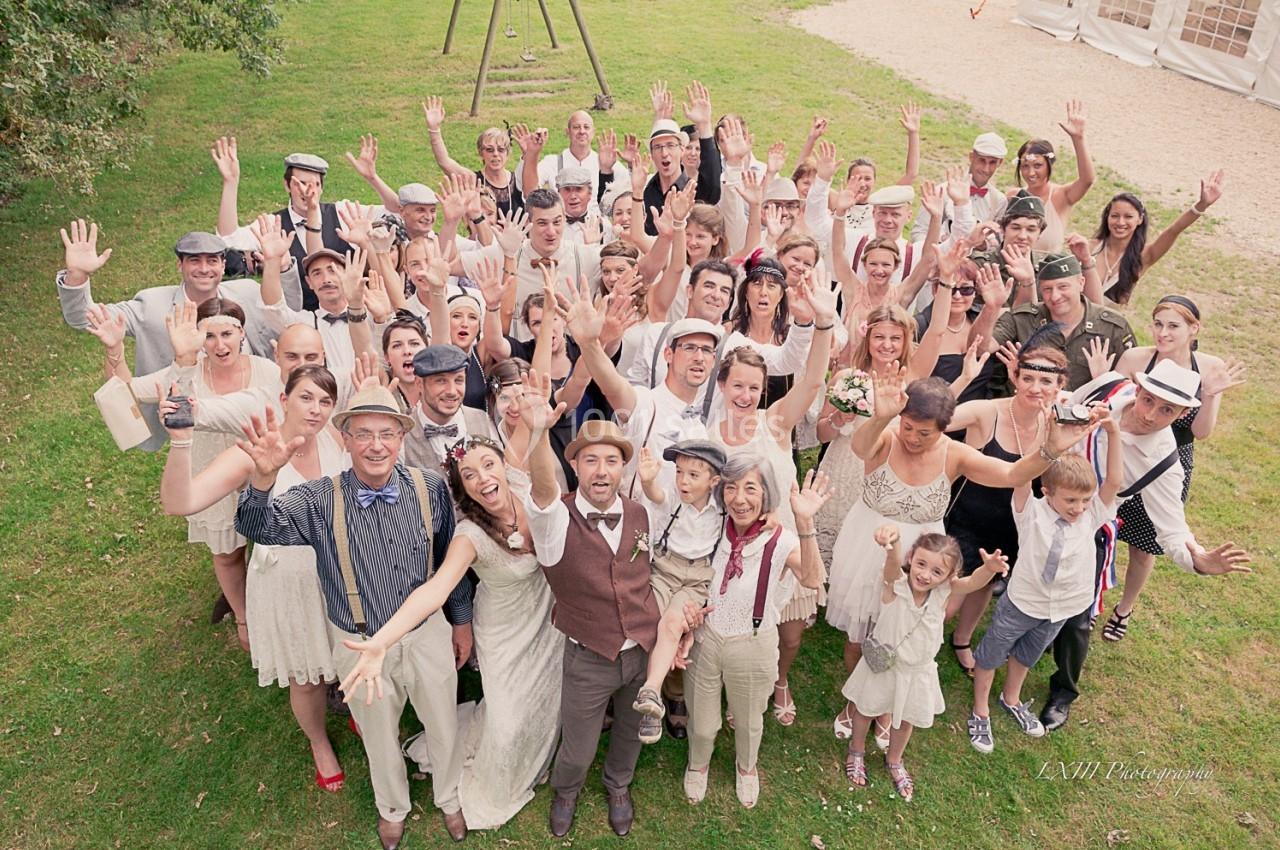 Groupe de personnes en tenue rétro souriant et levant les bras dans un espace extérieur verdoyant.