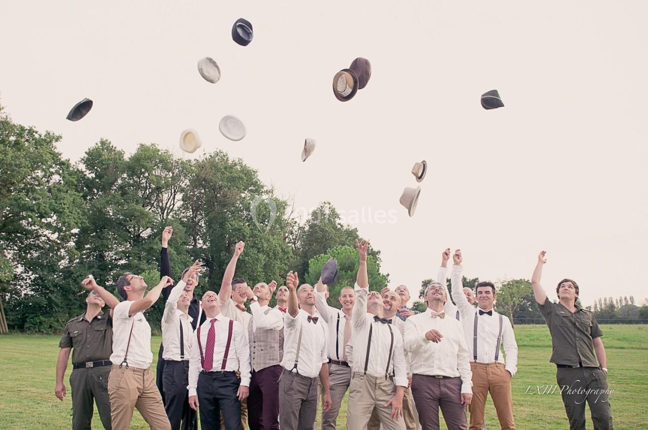 Un groupe d'hommes en tenue élégante lance des chapeaux en l'air dans un champ verdoyant.