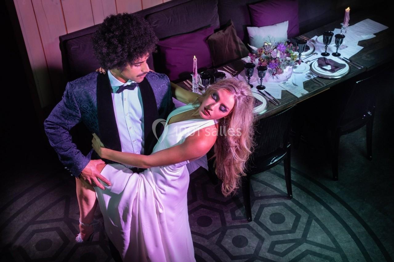 Un couple en tenue de soirée danse près d'une table élégamment dressée dans une ambiance tamisée.