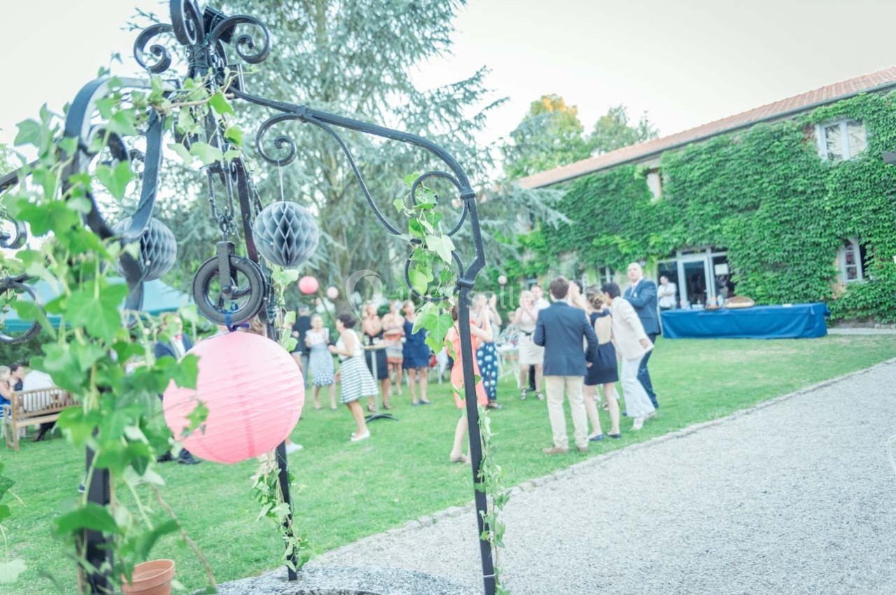 Location salle Roanne (Loire) - Château de Matel #6 Groupe de personnes discutant dans un jardin, décoré de lanternes et de végétation, près d'un bâtiment couvert de lierre.