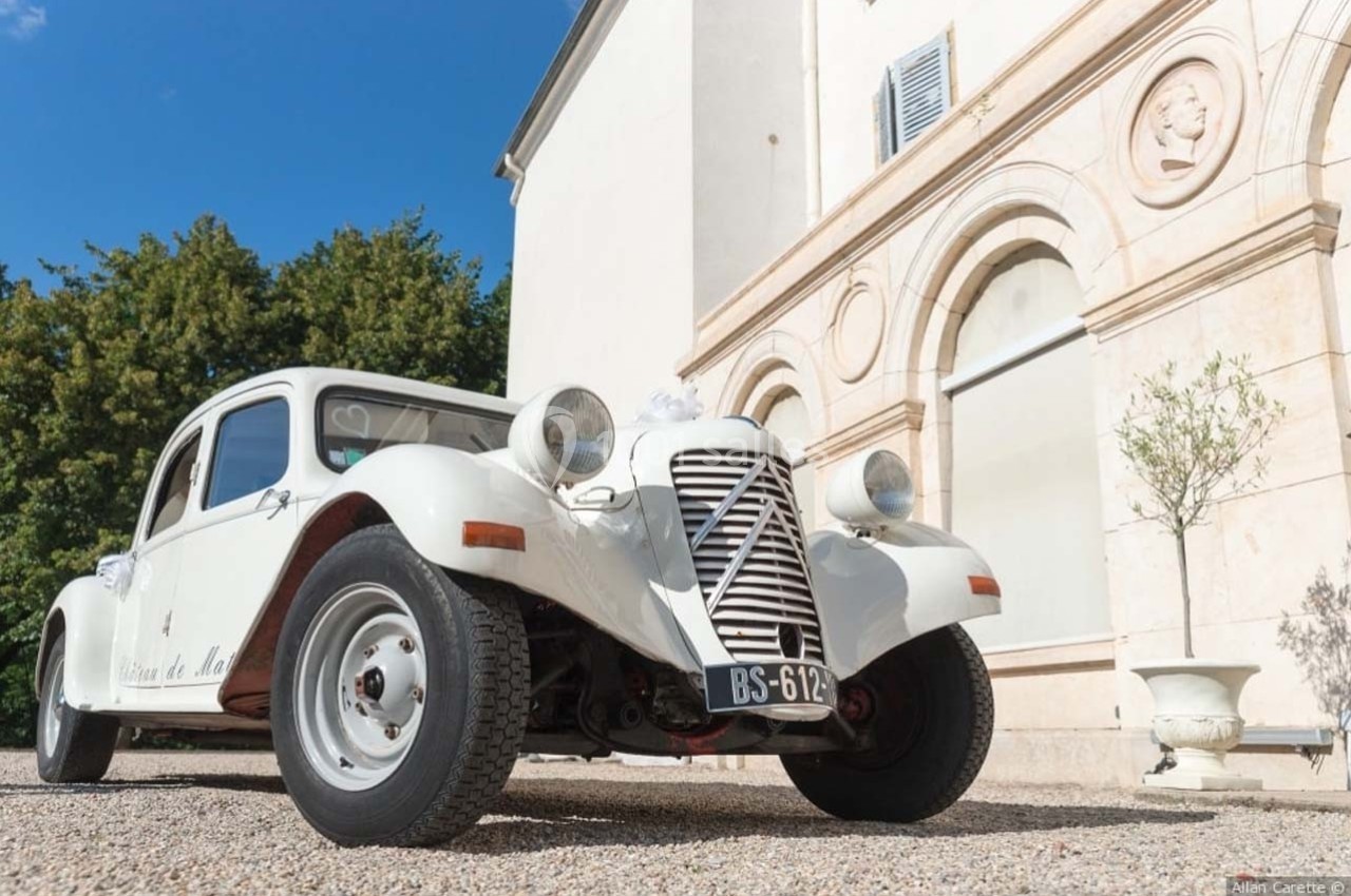 Location salle Roanne (Loire) - Château de Matel #29 Voiture ancienne blanche stationnée devant un bâtiment clair avec des arches et des arbres en arrière-plan.