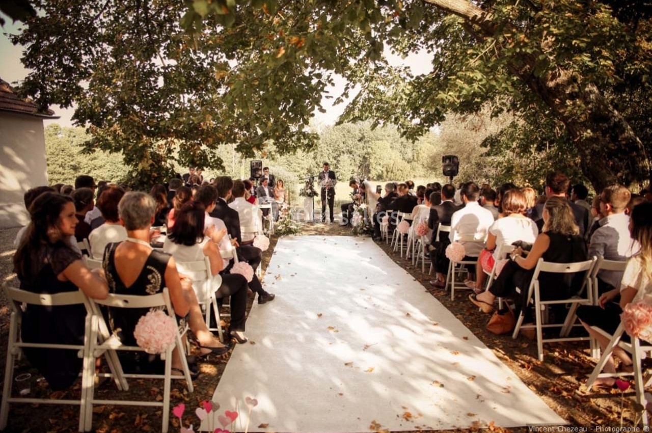 Location salle Roanne (Loire) - Château de Matel #26 Cérémonie de mariage en plein air avec des invités assis sous des arbres, face à un officiant.