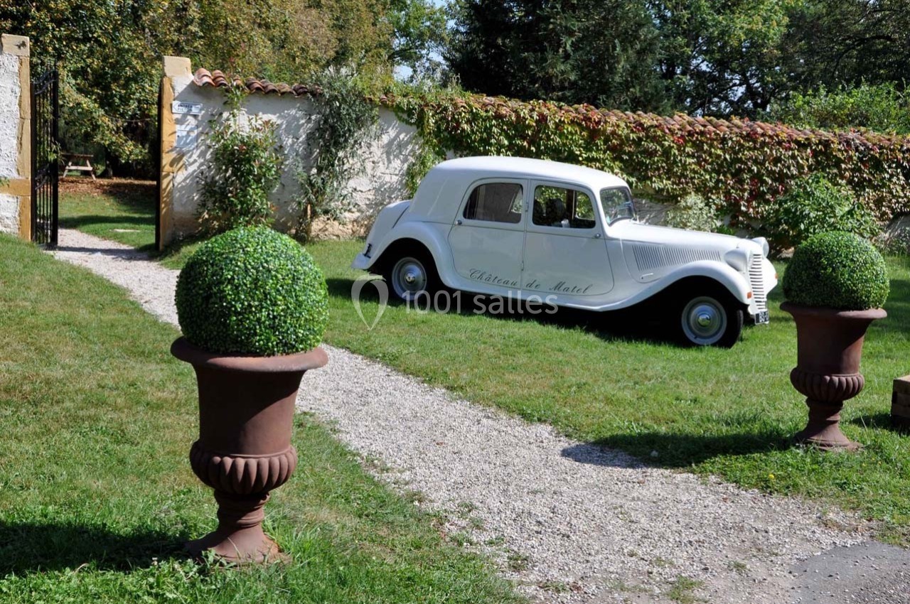 Location salle Roanne (Loire) - Château de Matel #36 Voiture ancienne blanche stationnée sur une allée gravillonnée, entourée de verdure et de buissons taillés.