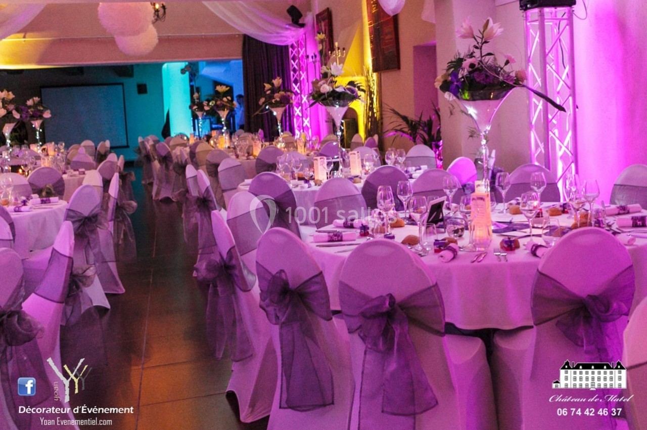 Location salle Roanne (Loire) - Château de Matel #11 Salle de réception décorée avec des tables rondes, nappes blanches, chaises ornées de nœuds violets et éclairage coloré.