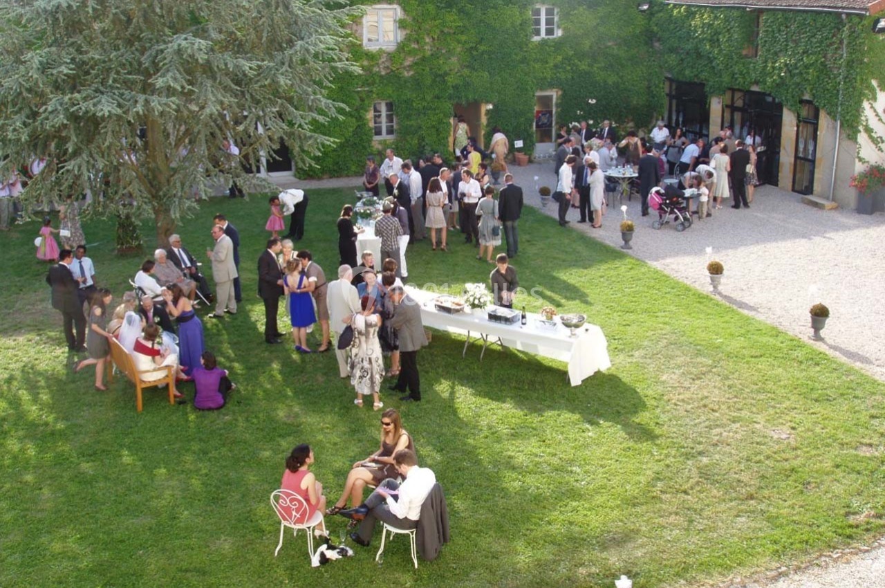 Location salle Roanne (Loire) - Château de Matel #33 Groupe de personnes rassemblées dans un jardin pour une réception, avec tables et bâtiments en arrière-plan.