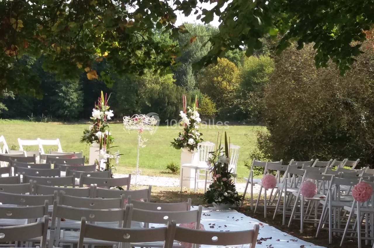 Location salle Roanne (Loire) - Château de Matel #27 Chaises blanches alignées en extérieur, décorées de fleurs, face à une arche florale dans un cadre verdoyant.