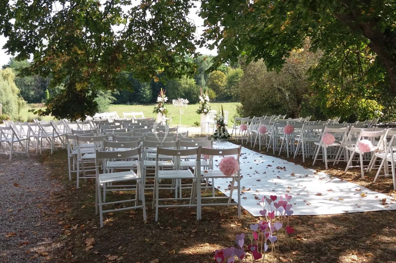 Location salle Roanne (Loire) - Château de Matel #28 Allée décorée pour une cérémonie en plein air, entourée de chaises blanches et de fleurs roses sous des arbres.