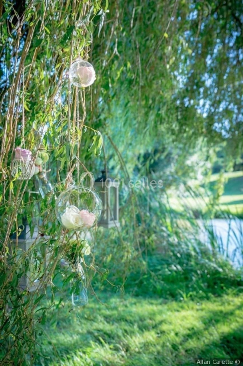 Location salle Roanne (Loire) - Château de Matel #34 Des fleurs roses et blanches suspendues dans des globes en verre, accrochés à un saule près d'un étang.