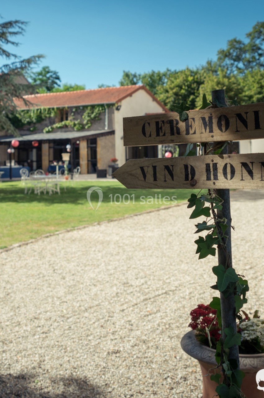 Location salle Roanne (Loire) - Château de Matel #4 Panneau en bois indiquant ’Cérémonie’ et ’Vin d'honneur’ dans un jardin devant un bâtiment avec terrasse.