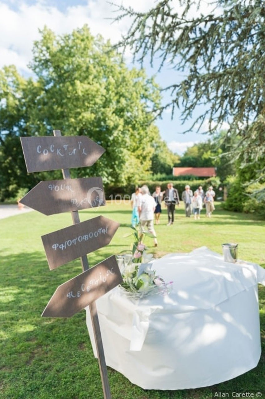 Location salle Roanne (Loire) - Château de Matel #21 Panneaux directionnels en bois sur une pelouse, avec une table décorée et des invités en arrière-plan.
