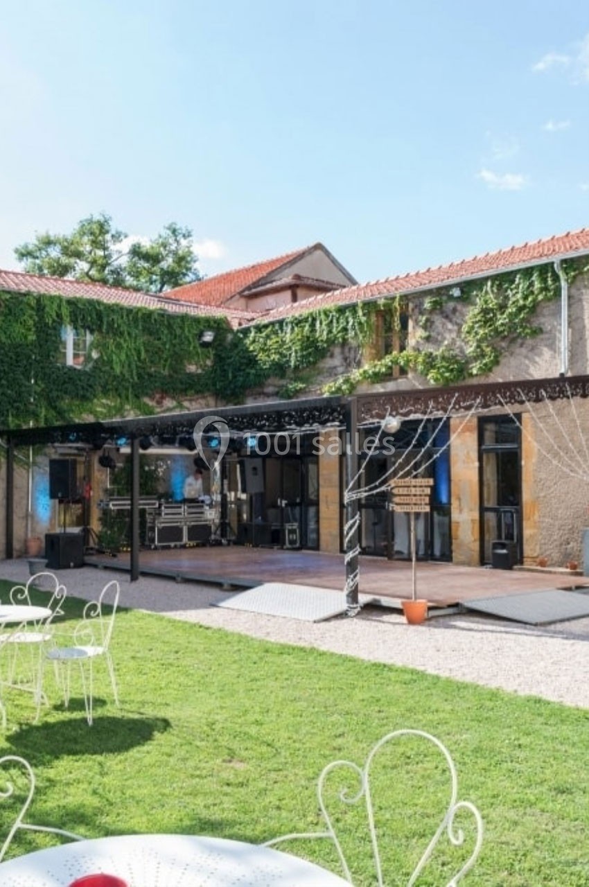 Location salle Roanne (Loire) - Château de Matel #43 Cour extérieure avec pelouse, mobilier de jardin blanc, scène équipée pour un événement, bâtiment en pierre et lierre.