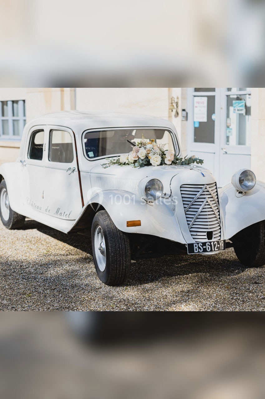 Location salle Roanne (Loire) - Château de Matel #44 Voiture ancienne blanche décorée de fleurs blanches et roses, stationnée devant un bâtiment clair.