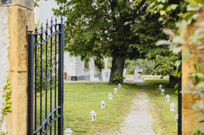 Miniature Location salle Roanne (Loire) - Château de Matel #45 Allée gravillonnée bordée de lanternes blanches menant à un jardin arboré, vue depuis un portail en fer forgé.