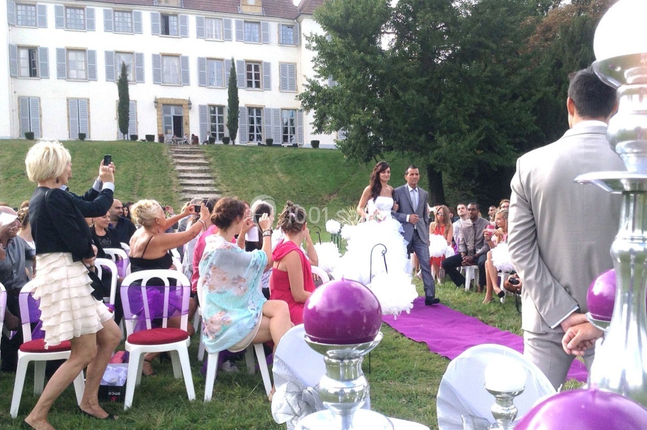 Location salle Roanne (Loire) - Château de Matel #41 Un couple marche sur un tapis violet lors d'une cérémonie de mariage en plein air devant une grande maison.