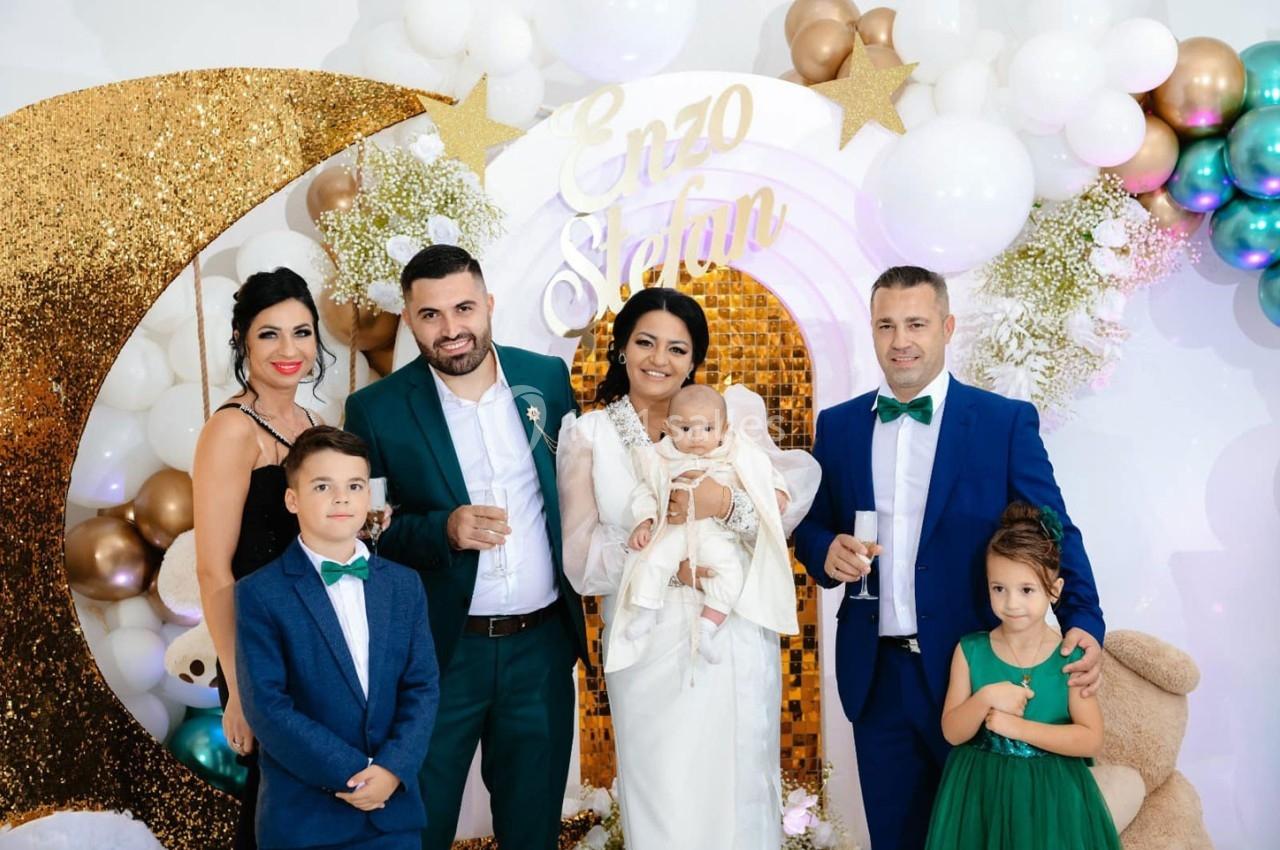 Un groupe de personnes posant devant une décoration festive avec des ballons, une arche dorée et un prénom affiché.