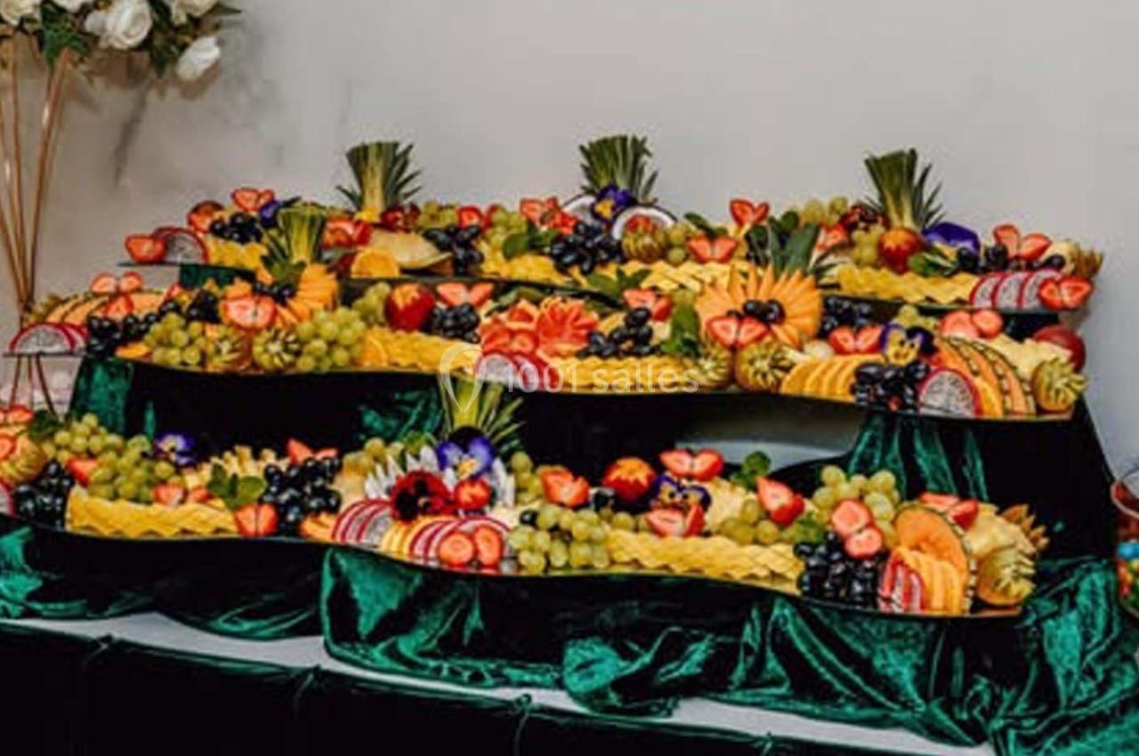 Plateaux garnis de fruits variés, dont ananas, fraises, raisins et agrumes, disposés sur une nappe verte.