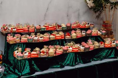 Présentation de desserts variés, notamment des cupcakes et gâteaux, disposés sur des étagères recouvertes de tissu vert.