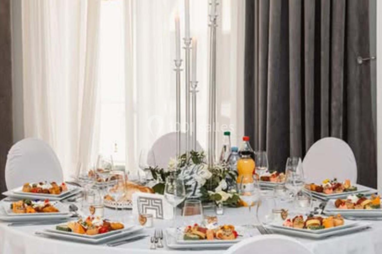 Table ronde élégamment dressée avec nappes blanches, chandeliers, assiettes garnies et boissons variées.