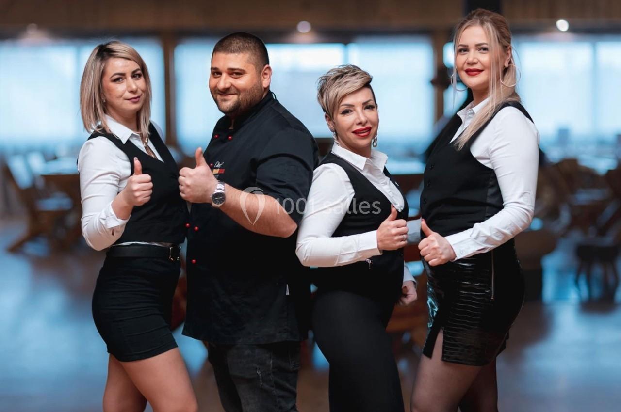 Quatre personnes en tenue professionnelle posent debout dans un espace intérieur, souriantes et levant le pouce.