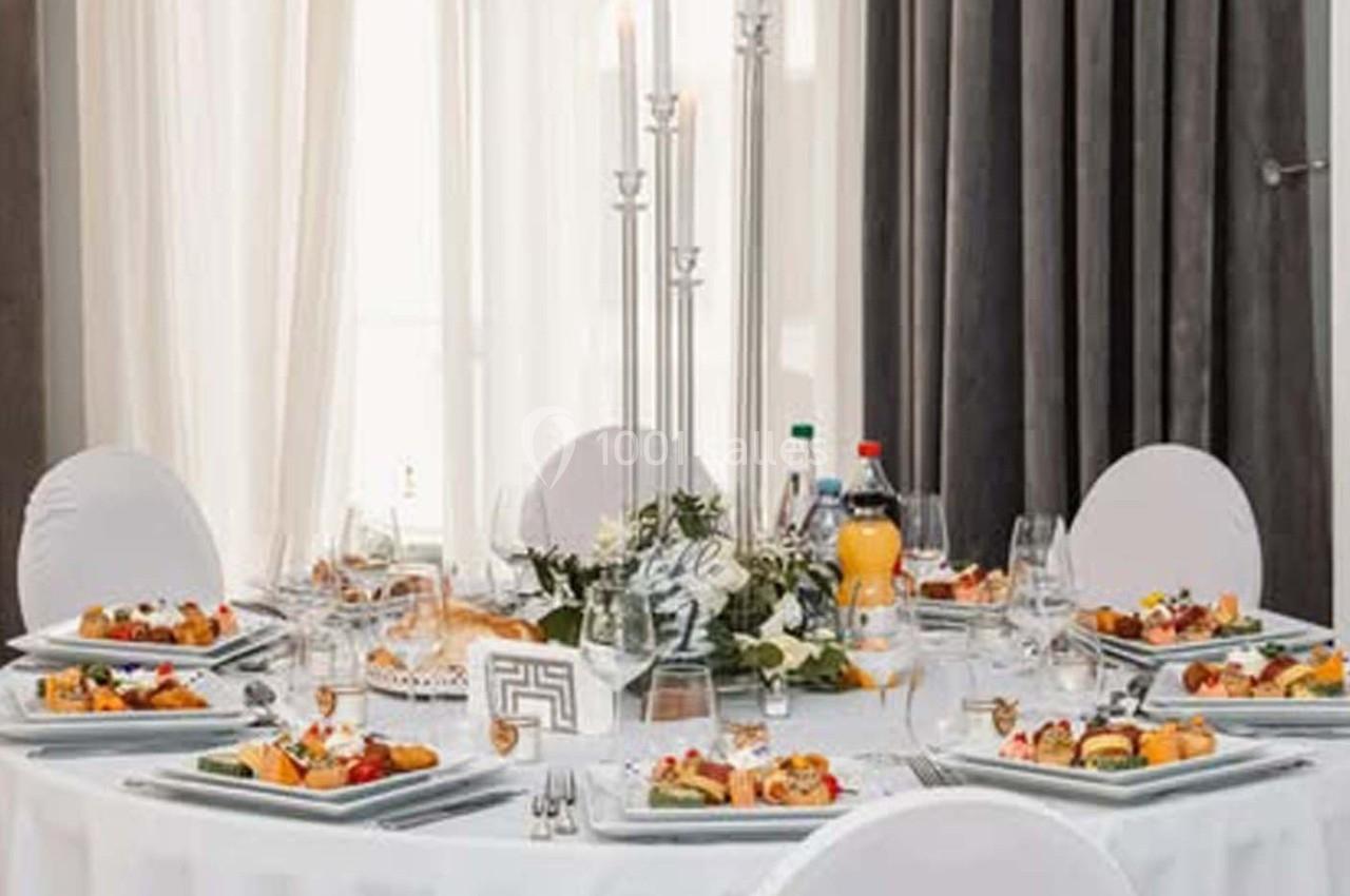 Table ronde élégamment dressée avec nappes blanches, chandeliers, assiettes garnies et décorations florales.