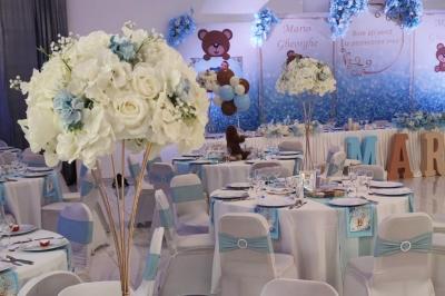 Salle de réception élégante avec un arc floral blanc, des tables décorées et un éclairage lumineux.