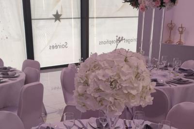 Salle de réception élégante avec un arc floral blanc, des tables décorées et un éclairage lumineux.
