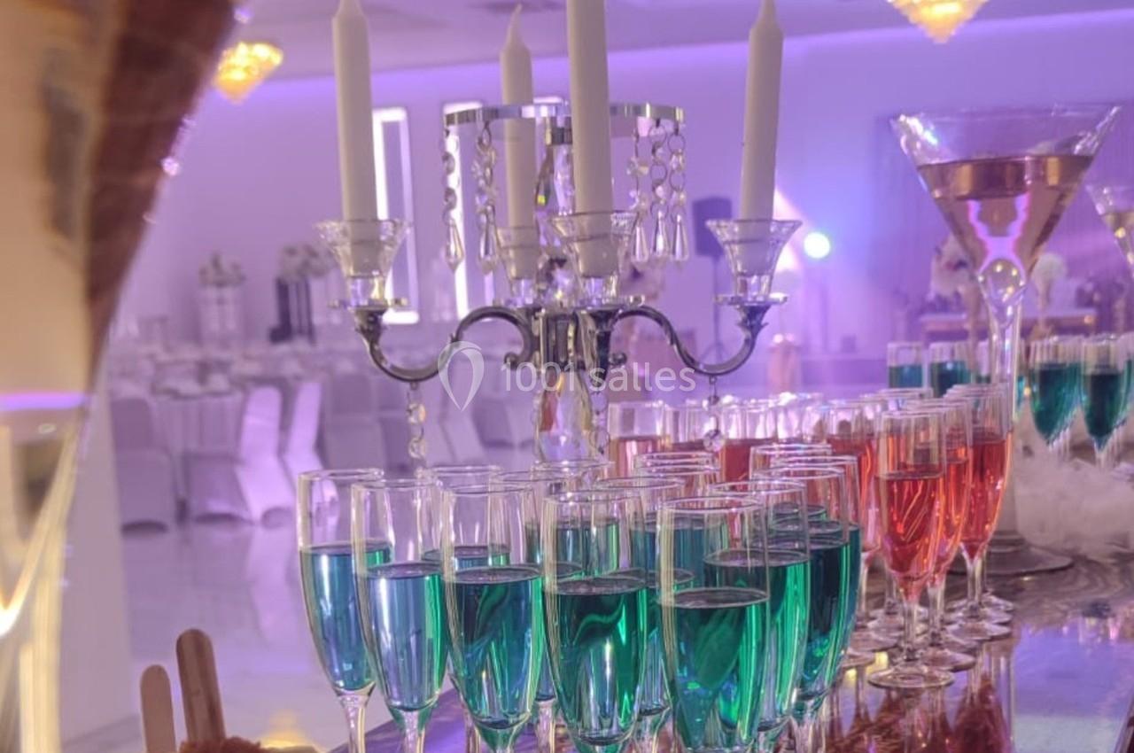 Bougies allumées sur un chandelier entouré de verres de cocktails colorés dans une salle de réception élégante.