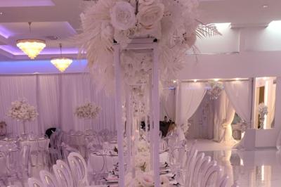 Salle de réception élégante avec un arc floral blanc, des tables décorées et un éclairage lumineux.