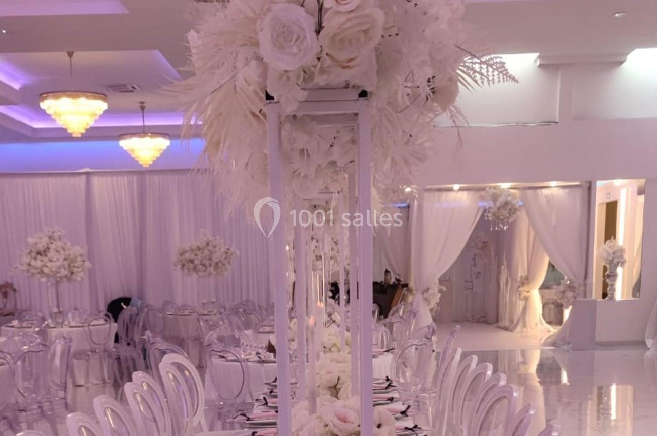 Salle de réception élégante avec décoration florale blanche, tables dressées et éclairage tamisé.