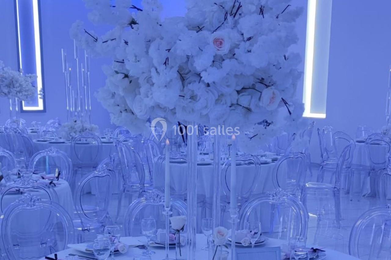 Centre de table avec des fleurs blanches sur une table dressée dans une salle lumineuse aux tons bleutés.