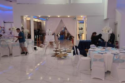 Salle de réception élégante avec un arc floral blanc, des tables décorées et un éclairage lumineux.