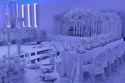 Salle de réception élégante avec un arc floral blanc, des tables décorées et un éclairage lumineux.