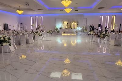 Salle de réception élégante avec un arc floral blanc, des tables décorées et un éclairage lumineux.
