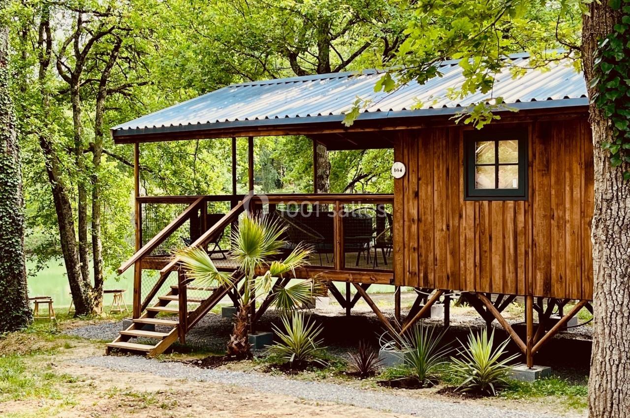 Cabane en bois sur pilotis entourée d'arbres, avec terrasse aménagée et vue sur un environnement naturel.