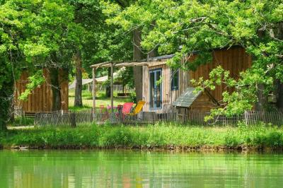 Table en bois décorée de fleurs, bougies et assiettes, installée en extérieur près d'un étang entouré d'arbres.