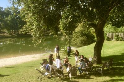 Table en bois décorée de fleurs, bougies et assiettes, installée en extérieur près d'un étang entouré d'arbres.