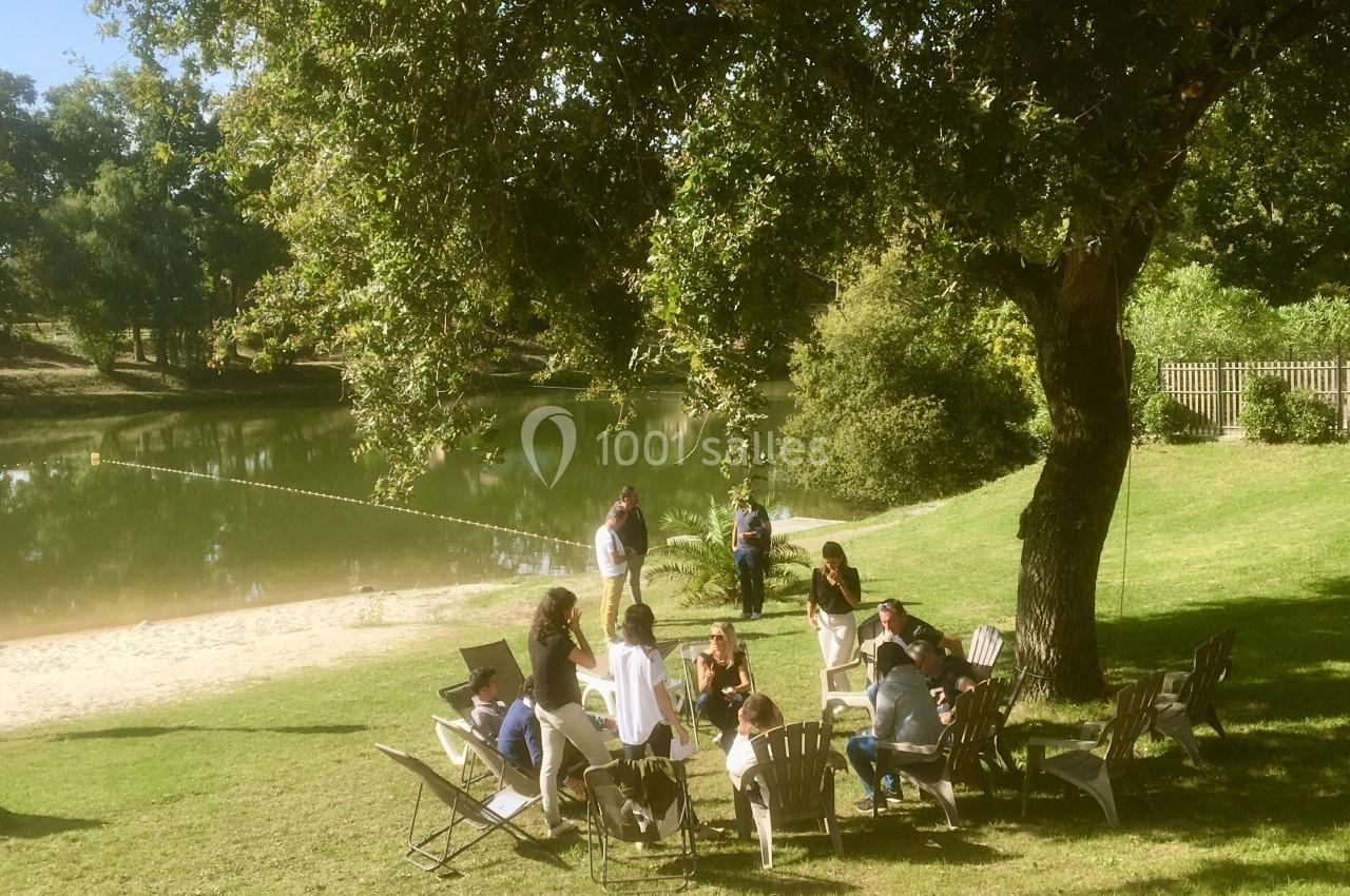 Un groupe de personnes assises sur des chaises en plein air près d'un lac entouré de verdure.