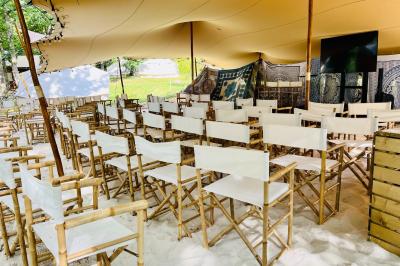 Table en bois décorée de fleurs, bougies et assiettes, installée en extérieur près d'un étang entouré d'arbres.
