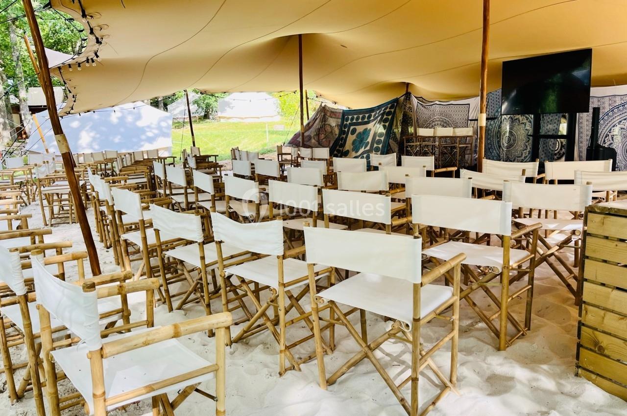 Chaises pliantes en bois avec assises blanches disposées sous une tente beige dans un espace extérieur sur du sable.