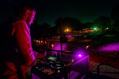 Table en bois décorée de fleurs, bougies et assiettes, installée en extérieur près d'un étang entouré d'arbres.