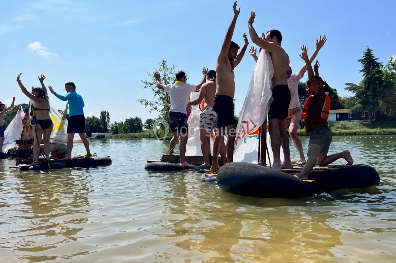 Des personnes debout sur des radeaux improvisés lèvent les bras dans un lac par une journée ensoleillée.