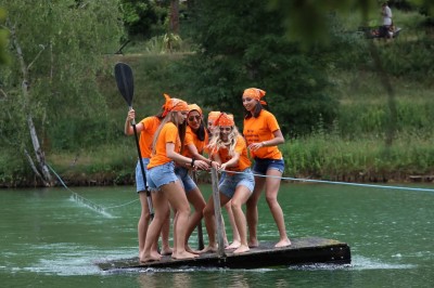 Table en bois décorée de fleurs, bougies et assiettes, installée en extérieur près d'un étang entouré d'arbres.
