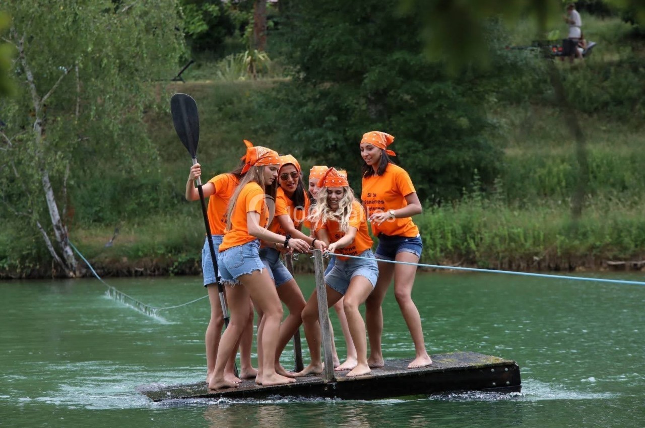 Un groupe de jeunes femmes en t-shirts orange sur un radeau flottant sur une rivière entourée de verdure.