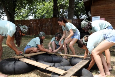 Table en bois décorée de fleurs, bougies et assiettes, installée en extérieur près d'un étang entouré d'arbres.