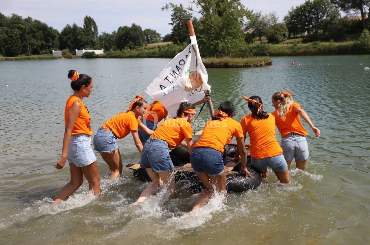 Un groupe de personnes en t-shirts orange pousse un radeau improvisé dans un lac par une journée ensoleillée.