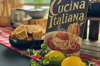 Table en bois décorée de fleurs, bougies et assiettes, installée en extérieur près d'un étang entouré d'arbres.