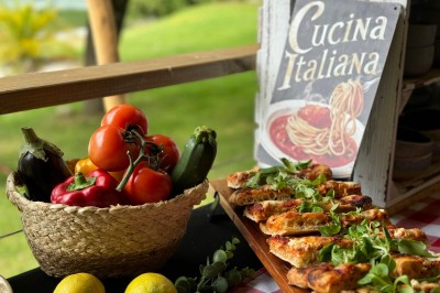 Table en bois décorée de fleurs, bougies et assiettes, installée en extérieur près d'un étang entouré d'arbres.